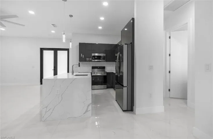 Kitchen featuring dark cabinets, modern cabinets, stainless steel appliances, pendant lighting, and light stone counters