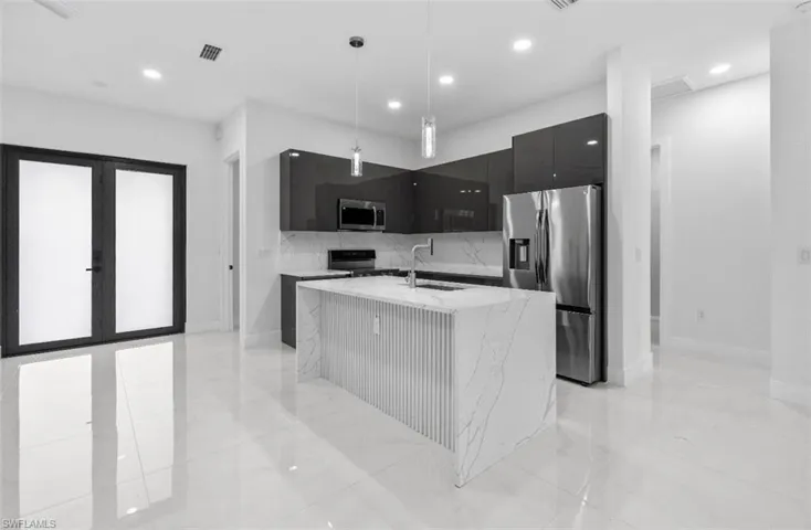 Kitchen featuring modern cabinets, dark cabinetry, stainless steel appliances, hanging light fixtures, and light stone countertops