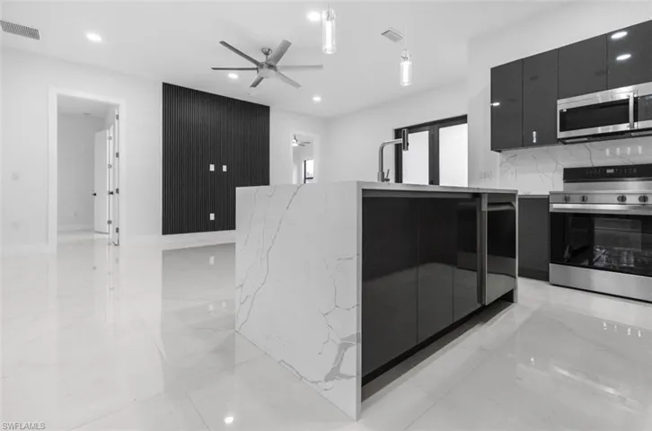 Kitchen with dark cabinetry, modern cabinets, stainless steel appliances, light stone countertops, and a ceiling fan