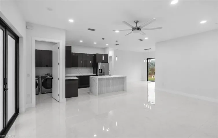 Kitchen featuring an island with sink, a ceiling fan, separate washer and dryer, dark cabinetry, and stainless steel refrigerator with ice dispenser