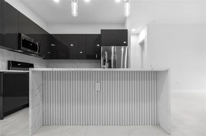 Kitchen with dark cabinetry, modern cabinets, an island with sink, stainless steel fridge, and recessed lighting
