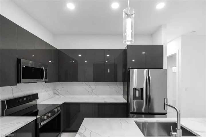 Kitchen with stainless steel appliances, modern cabinets, light stone countertops, and dark cabinetry