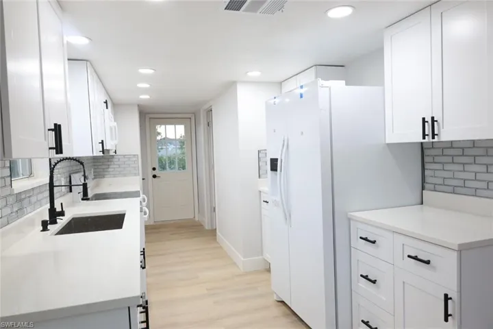 Kitchen featuring decorative backsplash, white cabinetry, white fridge with ice dispenser, light wood-style flooring, and recessed lighting