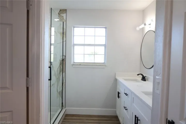 Bathroom featuring a marble finish shower, double vanity, and dark wood-style flooring