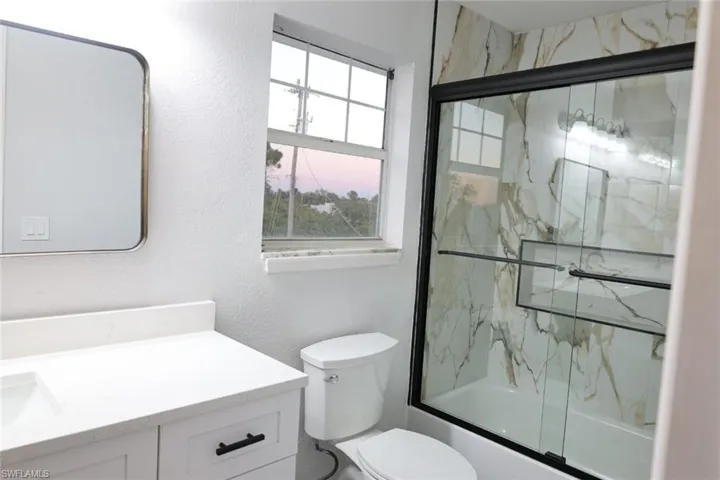 Full bathroom with shower / bath combination with glass door, vanity, and a textured wall
