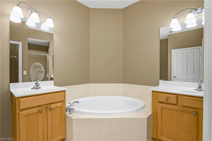 Full bath featuring two vanities, a chandelier, a garden tub, and a shower stall