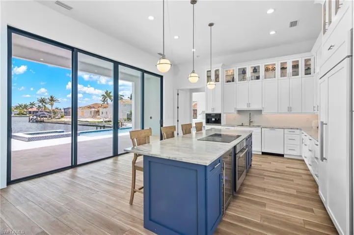 Kitchen with light hardwood / wood-style floors, decorative light fixtures, a kitchen island, backsplash, and white cabinets