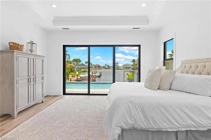 Bedroom featuring a water view, access to exterior, a tray ceiling, and light wood-type flooring