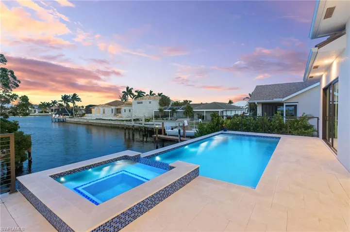 Pool at dusk featuring a patio, an in ground hot tub, and a water view
