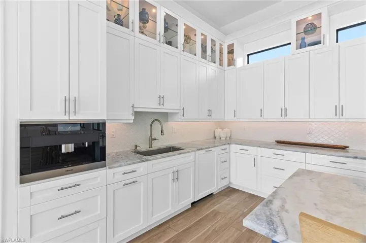Kitchen featuring light stone countertops, sink, white cabinets, and backsplash