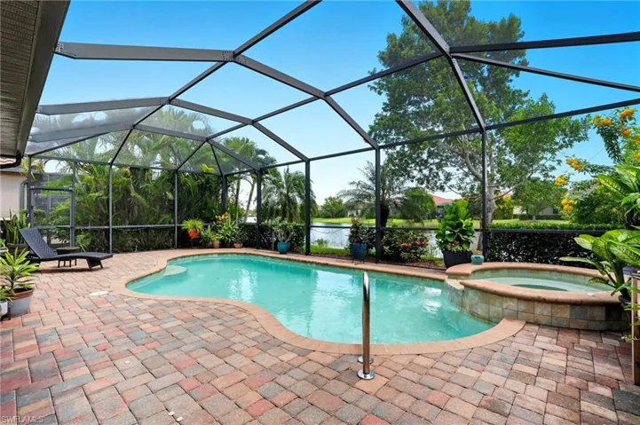 View of swimming pool with a sunroom, glass enclosure, a pool with connected hot tub, a water view, and a patio