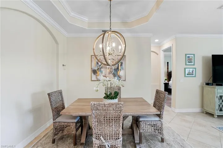 Dining space featuring arched walkways, ornamental molding, a chandelier, a raised ceiling, and light tile patterned floors