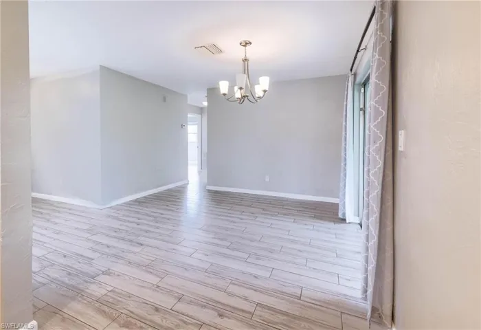 Empty room with light hardwood / wood-style flooring and an inviting chandelier