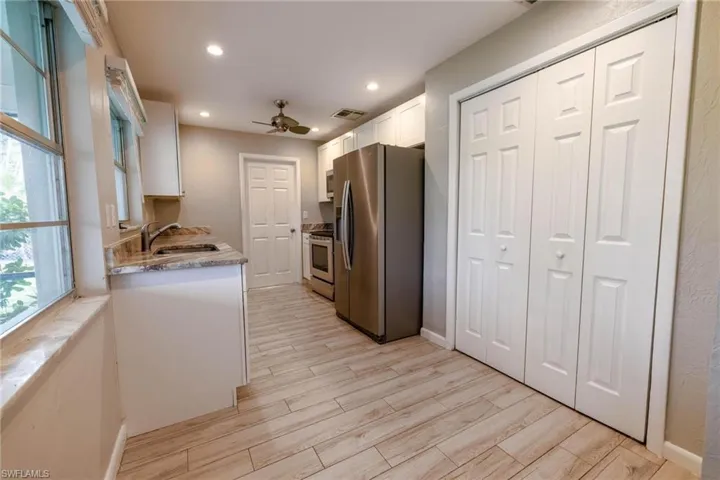 Kitchen with stainless steel appliances, ceiling fan, sink, white cabinets, and light hardwood / wood-style floors