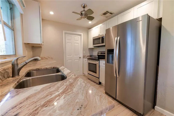 Kitchen featuring white cabinets, sink, ceiling fan, appliances with stainless steel finishes, and light stone counters