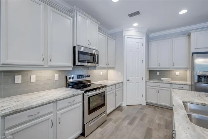 Kitchen with stainless steel appliances, white cabinets, decorative backsplash, and light stone countertops