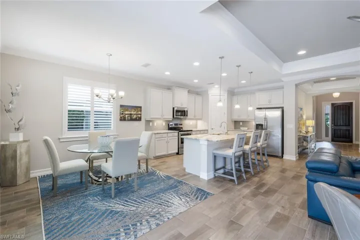 Kitchen with a chandelier, a center island with sink, stainless steel appliances, white cabinetry, and decorative light fixtures