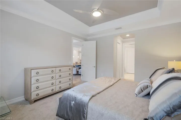 Carpeted bedroom with ceiling fan, a tray ceiling, and crown molding
