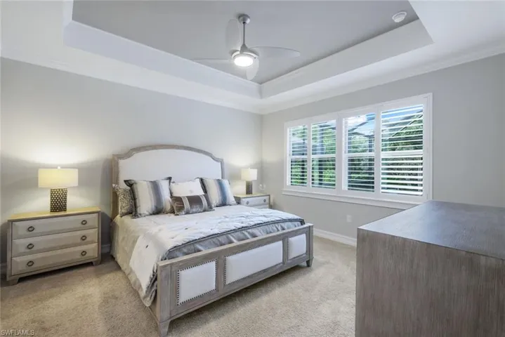 Bedroom featuring ceiling fan, light carpet, and a tray ceiling