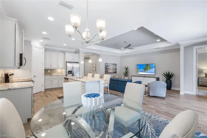 Dining room with light hardwood / wood-style flooring, a raised ceiling, ceiling fan with notable chandelier, ornamental molding, and sink