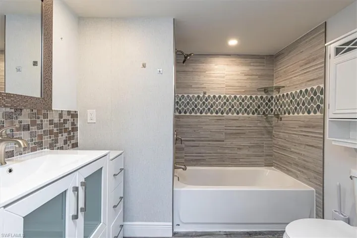 Bathroom featuring tub / shower combination, tile walls, vanity, tasteful backsplash, and recessed lighting