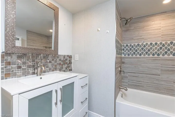 Bathroom with bathtub / shower combination, vanity, and tasteful backsplash
