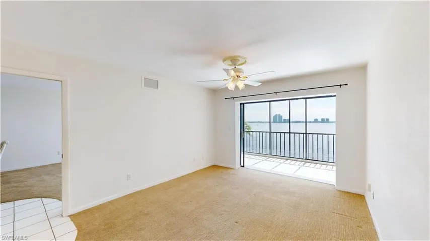 Empty room featuring light colored carpet, a water view, ceiling fan, and light tile patterned floors