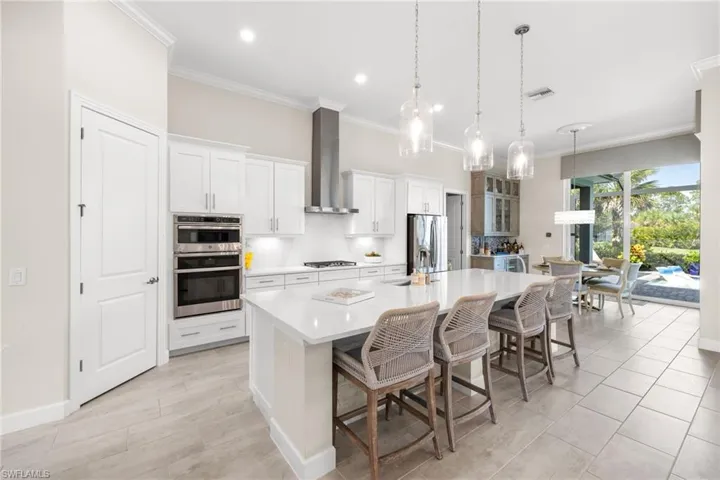 Kitchen featuring wall chimney range hood, a spacious island, a breakfast bar area, and appliances with stainless steel finishes
