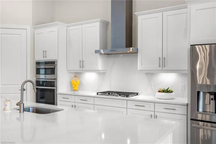 Kitchen featuring tasteful backsplash, stainless steel appliances, wall chimney exhaust hood, sink, and white cabinetry