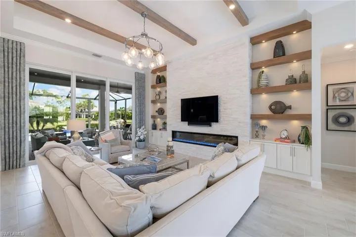 Tiled living room with built in features, beam ceiling, a notable chandelier, and a stone fireplace