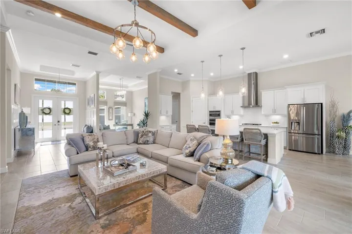 Living room with ornamental molding, french doors, beam ceiling, and a chandelier