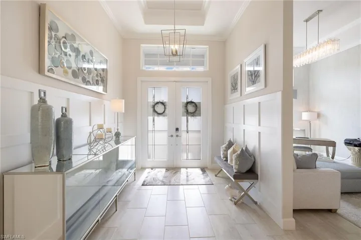 Foyer entrance with a notable chandelier, a raised ceiling, crown molding, a high ceiling, and french doors