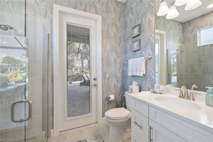 Bathroom featuring tile flooring, a shower with door, toilet, and large vanity