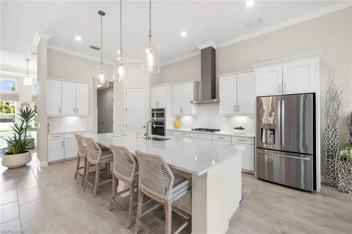Kitchen featuring stainless steel appliances, wall chimney range hood, a large island with sink, and white cabinets