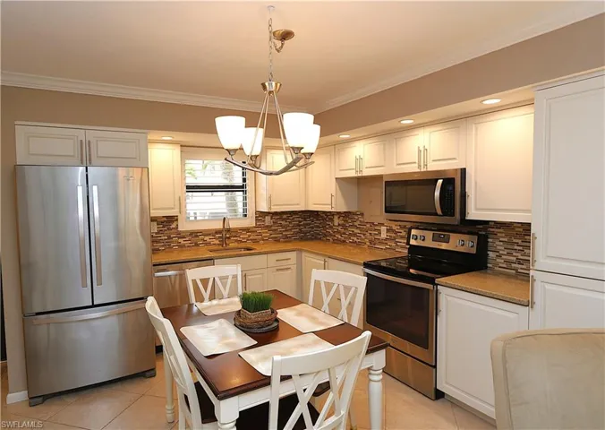Kitchen featuring ornamental molding, appliances with stainless steel finishes, white cabinets, pendant lighting, and tasteful backsplash