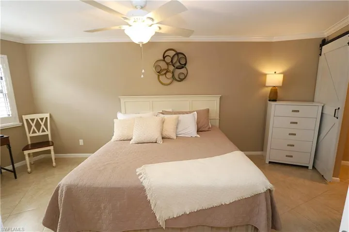 Bedroom featuring a barn door, light tile patterned flooring, crown molding, and ceiling fan