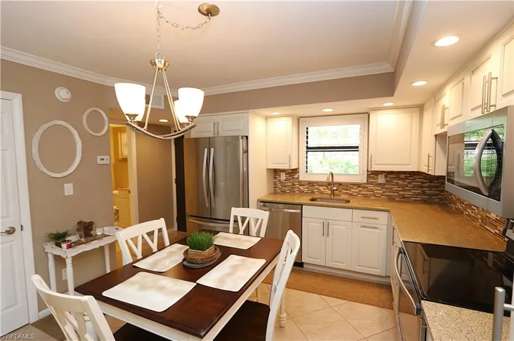 Kitchen featuring appliances with stainless steel finishes, tasteful backsplash, ornamental molding, light tile patterned flooring, and decorative light fixtures