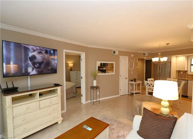 Living area with ornamental molding, light tile patterned floors, and a chandelier