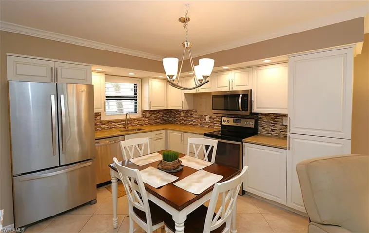 Kitchen featuring ornamental molding, appliances with stainless steel finishes, decorative light fixtures, a chandelier, and light tile patterned flooring