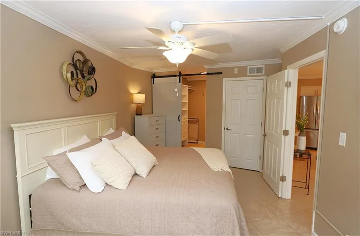Bedroom featuring a barn door, crown molding, light tile patterned floors, stainless steel refrigerator, and ceiling fan