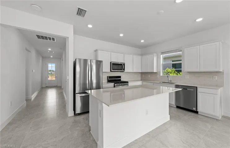 Kitchen featuring a center island, white cabinetry, appliances with stainless steel finishes, backsplash, and sink