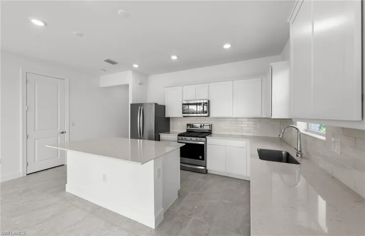 Kitchen with stainless steel appliances, sink, a center island, and tasteful backsplash