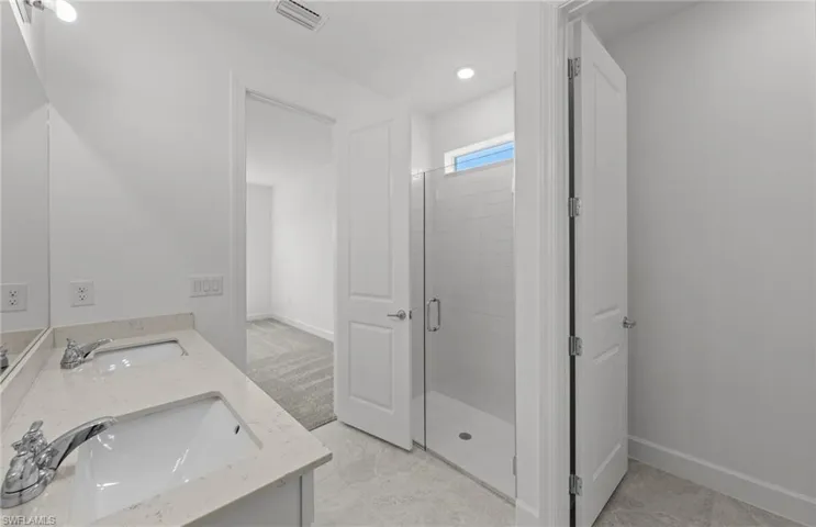Bathroom with tile floors, vanity with extensive cabinet space, a shower with shower door, and double sink