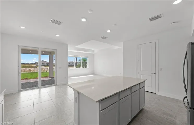 Kitchen with gray cabinetry, stainless steel fridge, a kitchen island, and light tile floors