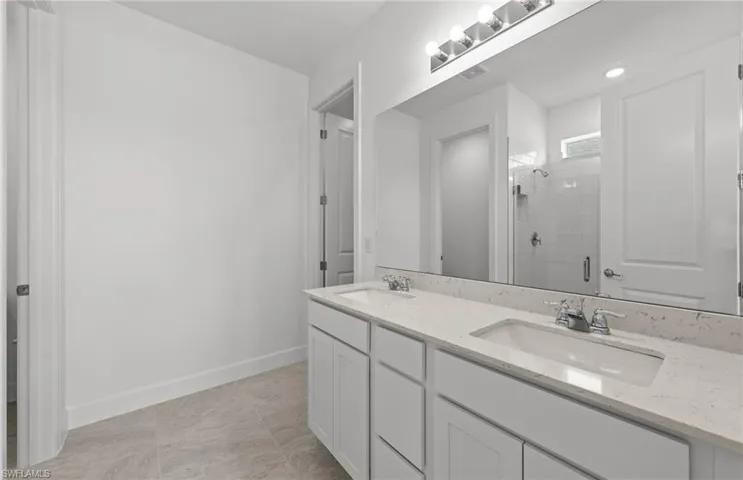 Bathroom featuring a shower with shower door, large vanity, double sink, and tile floors