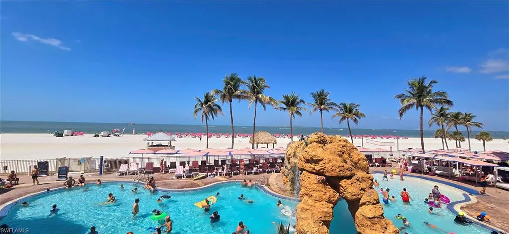 Community pool featuring a view of the beach, fence, and a water view