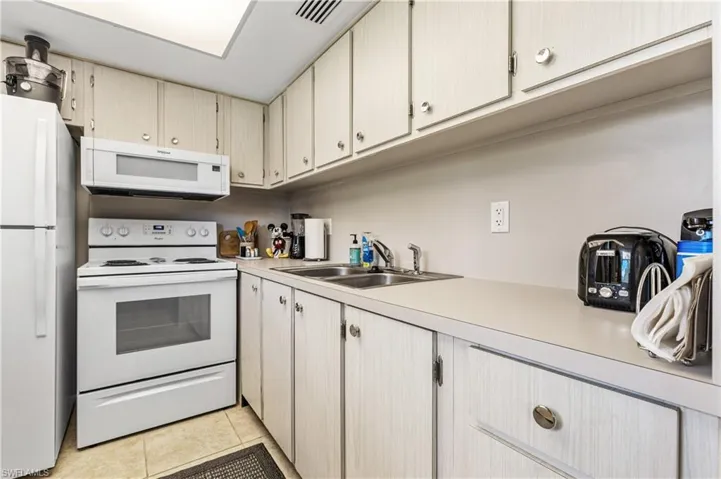 Kitchen with white appliances, a sink, light countertops, and light tile patterned flooring