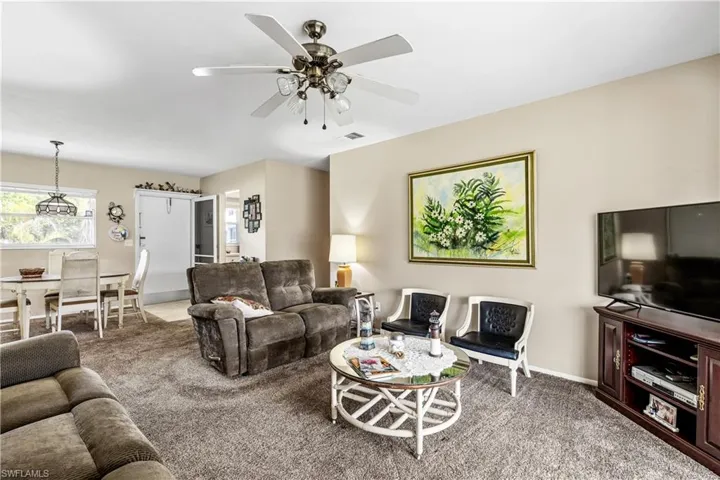 Carpeted living room featuring ceiling fan and baseboards