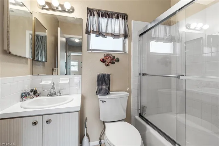 Full bath with a textured wall, toilet, enclosed tub / shower combo, and vanity