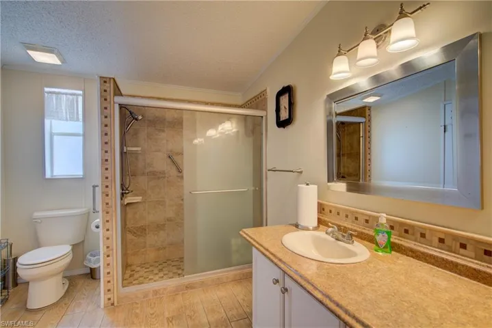 Full bathroom featuring a textured ceiling, vanity, crown molding, a shower stall, and light wood finished floors